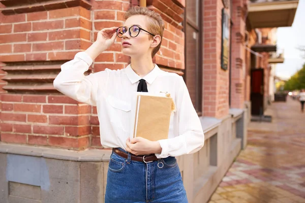 Krásná žena s krátkými vlasy drží zápisník v ruce a stojí v blízkosti cihlové budovy na ulici — Stock fotografie