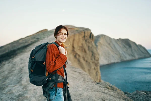 Glückliche Reisende Frau, die in den Bergen am Meer ruht und Rückenansicht eines Modell-Rucksacks — Stockfoto
