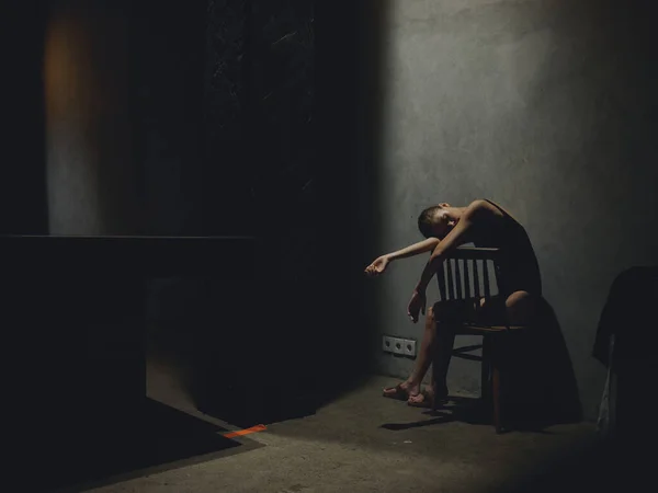 Une femme assise sur une chaise lève les jambes et s'appuie sur le côté sur un fond sombre silhouette d'un modèle — Photo