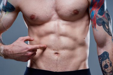 Karnında küpleri olan sporcu vücut kaslarını şişirmiş dövmeler çıplak gözle görünür.