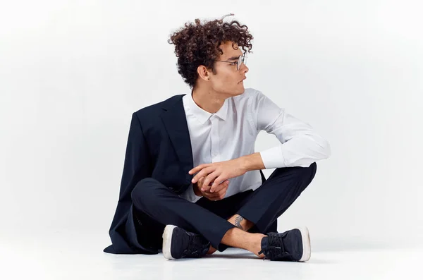 Συναισθηματική τύπος σε ένα κλασικό κοστούμι κάθεται στο πάτωμα σε ένα φωτεινό δωμάτιο γυαλιά στο πρόσωπο πορτρέτο μοντέλο — Φωτογραφία Αρχείου