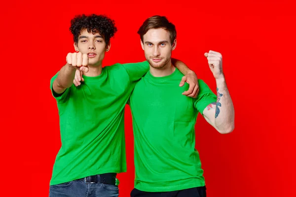 두 명의 쾌활 한 친구가 녹색 티셔츠의 감정을 껴 안 으며 빨간 배경의 의사소통을 한다 — 스톡 사진