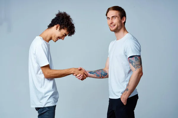 하얀 티셔츠를 입고 격리 된 배경을 가진 두 친구가 손을 잡고 있다 — 스톡 사진