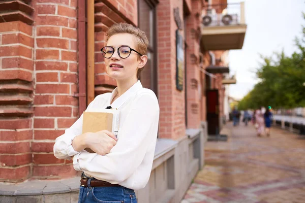 Femme près d'un bâtiment en brique dans des lunettes avec un livre dans ses mains sur l'institut d'éducation de la rue — Photo