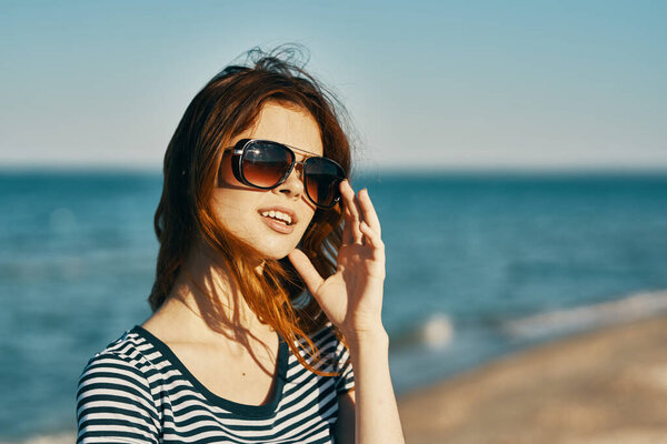женщина в футболке и очках прогуливается по песчаному берегу на пляже у синего моря