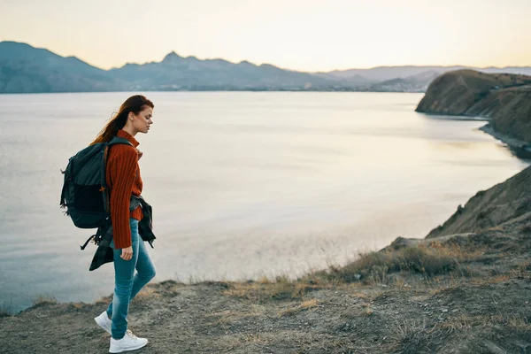 Мандрівник в светрі з рюкзаком в джинсах і кросівки на пляжі біля моря в горах — стокове фото