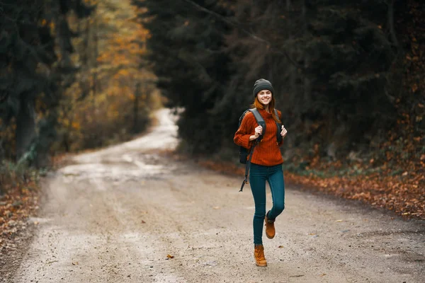 Donna con uno zaino in piena crescita cammina lungo la strada nel bosco in autunno — Foto Stock