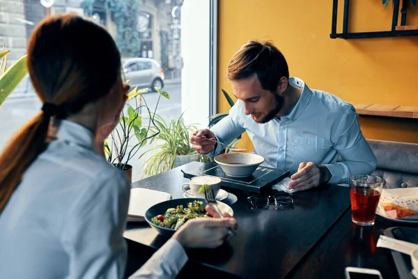 Um homem e uma mulher em uma camisa jantando em uma mesa em um restaurante interior no fundo bebidas de comida quente — Fotografia de Stock