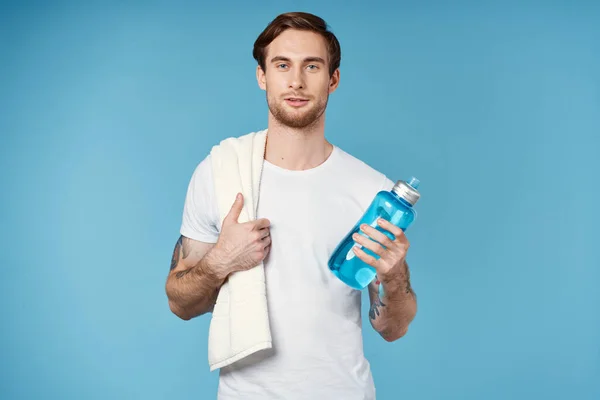 Спортсмен у білій футболці п'є пляшку енергії синій фон — стокове фото