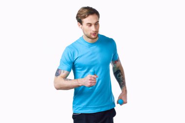 Bir adam elinde dambıllarla spor salonuna gider. Hafif bir arka plan ve dövme modeli.