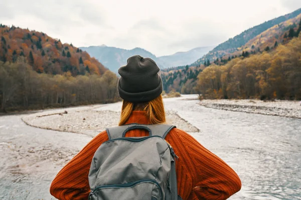 Kobieta w swetrze i czapce z plecakiem na plecach w górach na krajobrazie natury — Zdjęcie stockowe