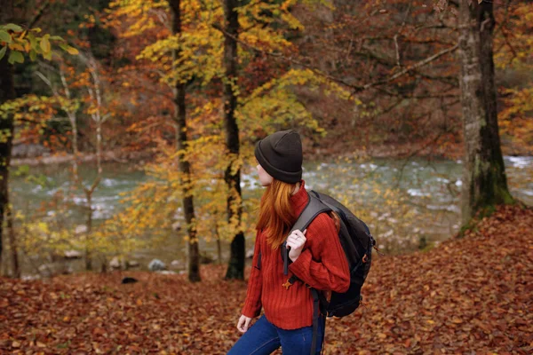 Zijaanzicht van gelukkige vrouw in park in de herfst nabij rivier en rugzak op haar rug — Stockfoto