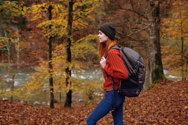Žena v podzimním parku s padlým listím a batohem na zádech řeky v pozadí — Stock fotografie