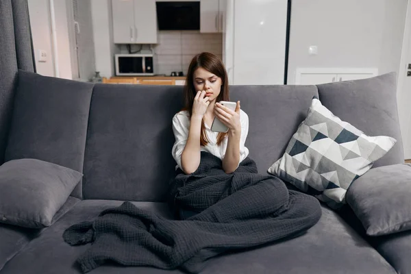 Mujer sentada en el sofá con el teléfono móvil descansando almohada interior —  Fotos de Stock