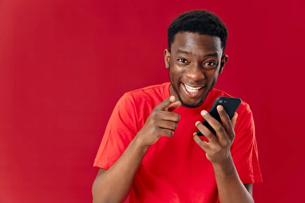 Homem alegre de aparência africana com telefone celular rindo no fundo vermelho — Fotografia de Stock