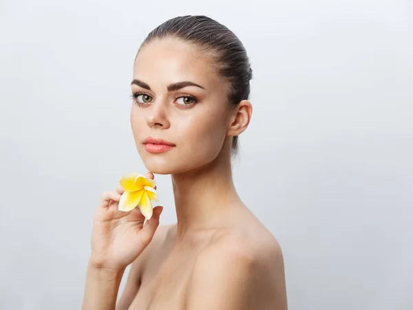 Beautiful woman holding a yellow flower in her hands on a light background — Stock Photo, Image