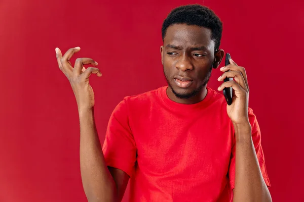 Afrikalı görünüşlü kırmızı tişörtlü adam telefonda konuşuyor. — Stok fotoğraf