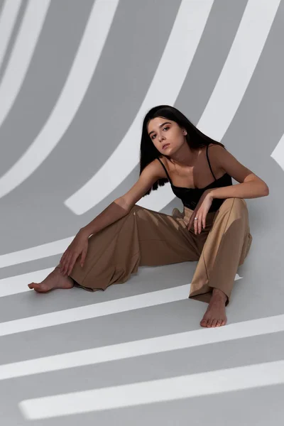 Una mujer está sentada en el suelo con ropa de moda y una sombra que cae no está en la pared —  Fotos de Stock