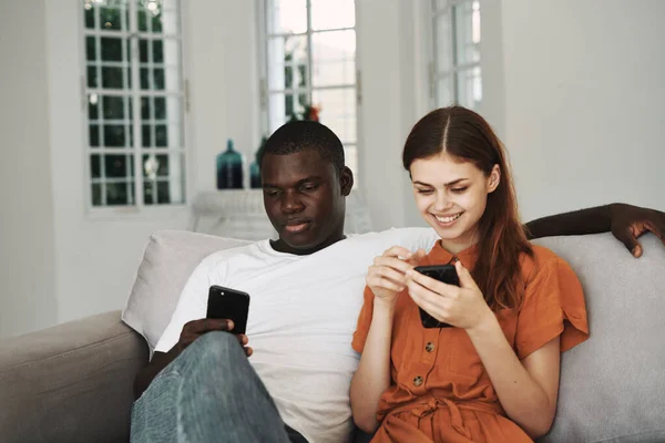 Un homme et une femme sont assis à la maison sur le canapé avec des téléphones dans leurs mains Internet — Photo