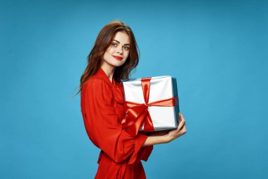 Elinde hediye kutusuyla kırmızı elbiseli bir kadın mavi arka planda yeni yılda