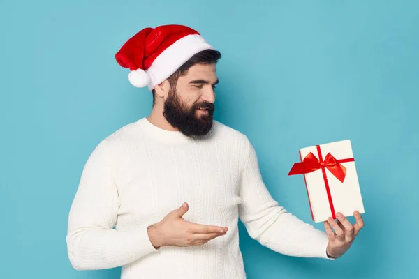 Hombre barbudo en suéter blanco sosteniendo una caja de regalo gorra de Navidad año nuevo — Foto de Stock