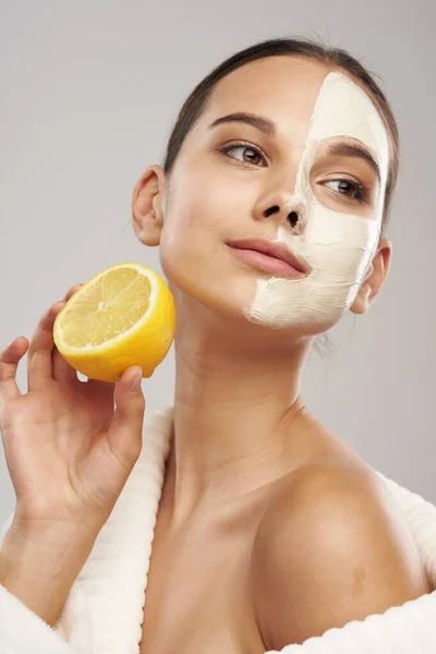 Woman in white coat lemon in hands mask on face clean skin cosmetics