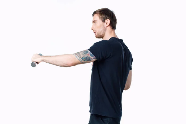 Hombre fuerte atleta en una camiseta negra haciendo ejercicios con pesas en sus manos fitness — Foto de Stock