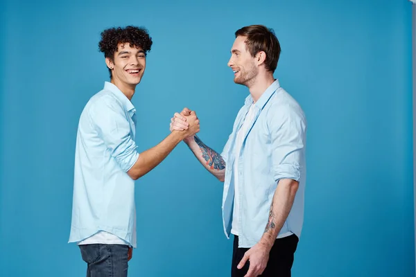 Счастливые друзья в одинаковых рубашках пожимают руки на синем фоне общения — стоковое фото