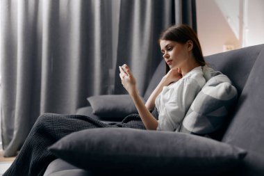 Kanepede oturan rahat bir kadın. Elinde telefon, iç mobilyaları var.