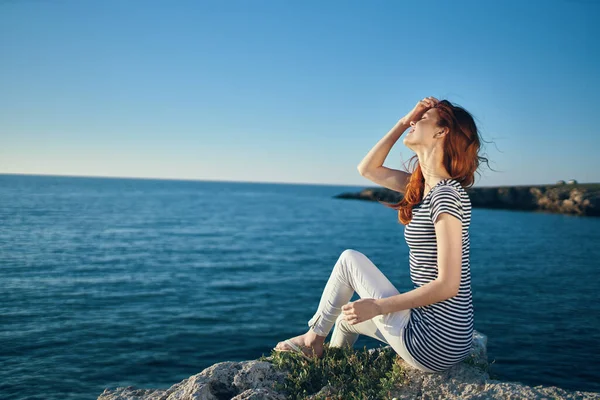 Donna in t-shirt e pantaloni si siede su una pietra vicino al mare in estate — Foto Stock