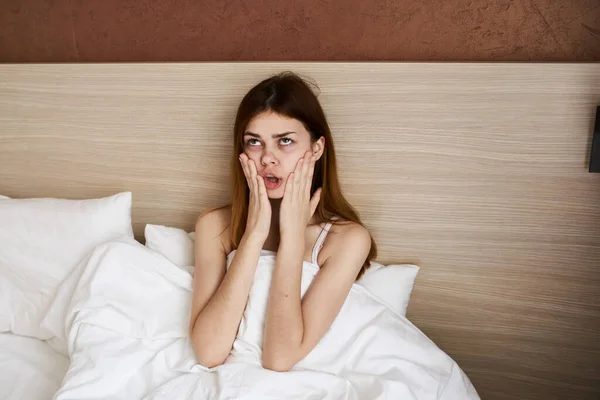 woman woke up early in the morning and touch her face with her hands under the covers in bed