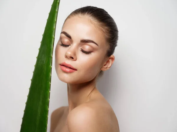 Mulher com olhos fechados e folha de aloés verde no fundo claro vista cortada — Fotografia de Stock