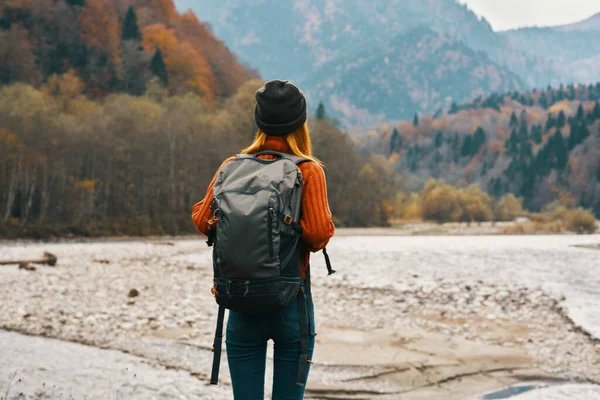 Mulher viaja nas montanhas no outono perto do rio na natureza com uma mochila vista para trás — Fotografia de Stock