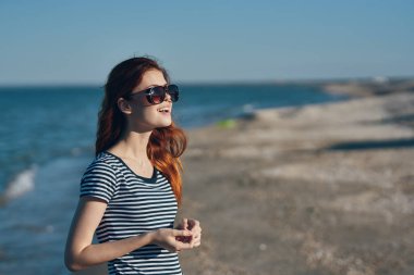 Yazın plajda yürüyen gözlüklü ve çizgili tişörtlü bir kadın.