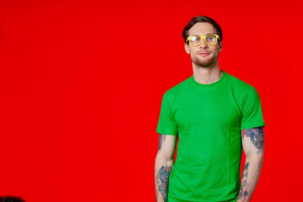 녹색 티셔츠를 입고 손에 문신을 하고 빨간 배경에 안경을 쓴 남자 — 스톡 사진
