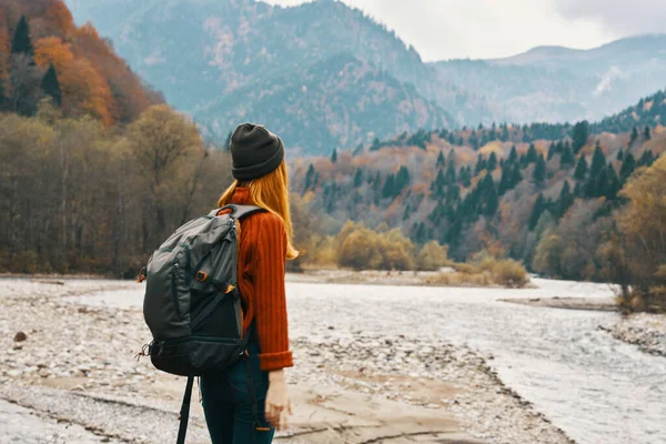 Um viajante com uma mochila em uma camisola e jeans estão descansando nas montanhas na natureza perto do rio no outono — Fotografia de Stock