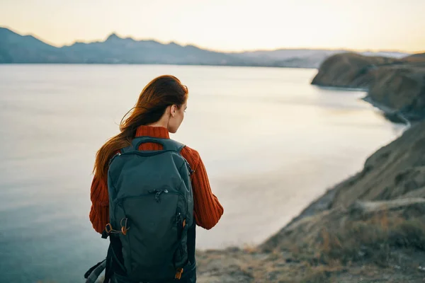 Donna in un maglione rosso con uno zaino sulla schiena in montagna sulla natura rocce alte paesaggio tramonto — Foto Stock