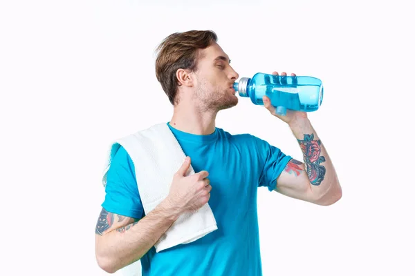 Atleta hombre bebe agua de una botella sobre un fondo blanco y una toalla en su hombro — Foto de Stock