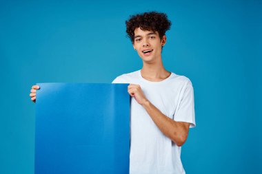 Beyaz tişörtlü bir adam elinde mavi arka plan reklamları yapan bir poster tutuyor.