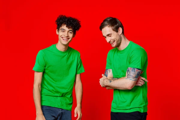 Due amici in t-shirt verdi sono in piedi fianco a fianco comunicazione positiva sfondo rosso — Foto Stock