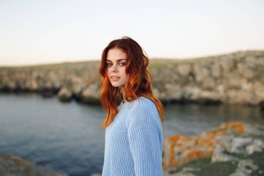 Açık havada kazak giyen kızıl saçlı kadın kayalık dağlarda tatil yapıyor.