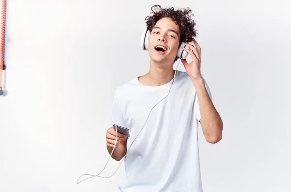 Beyaz tişörtlü, kıvırcık saçlı adam kulaklıklı telefon teknolojisiyle müzik dinliyor. — Stok fotoğraf