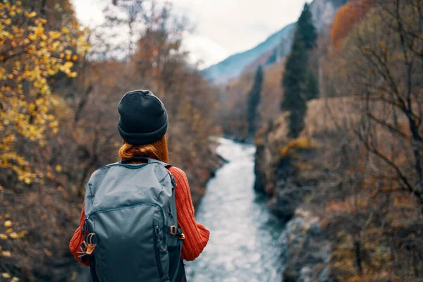 Mulher caminhante com uma mochila nas costas perto de um rio de montanha na natureza, vista para trás — Fotografia de Stock