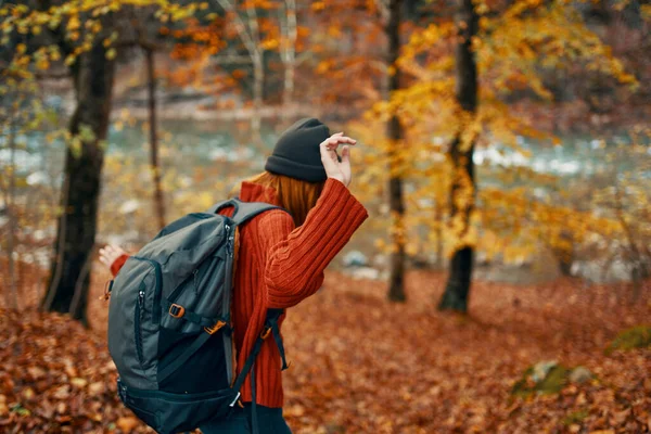 Žena ve svetru s batohem odpočívá v parku v blízkosti řeky v přírodě na podzim — Stock fotografie