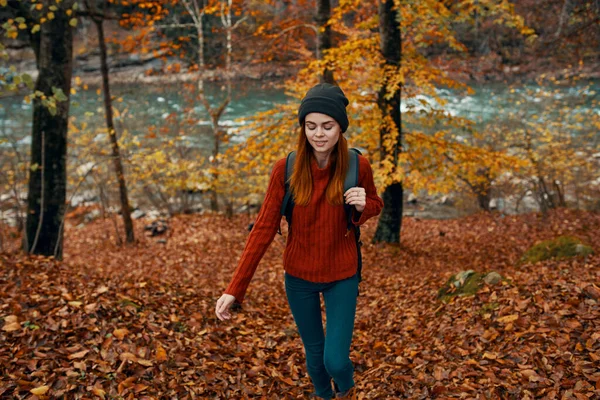 Mulher em uma camisola com uma mochila descansando em um parque perto do rio na natureza no outono — Fotografia de Stock