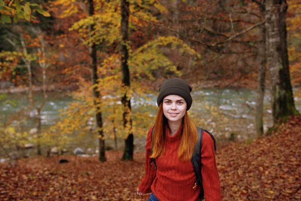 Ormanda sonbaharda uzun ağaçların yanında sırt çantalı kazaklı bir kadın turist. — Stok fotoğraf