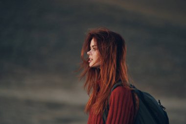 Sırtında bir sırt çantasıyla güzel bir seyahat ve bir süveter içinde dağların doğasına bakıyor.