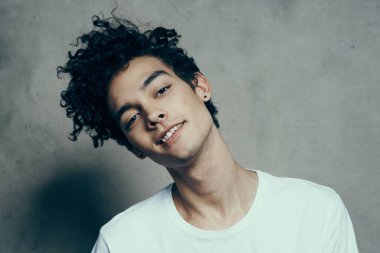 Kıvırcık saçlı neşeli adam gri arka plan fotostudio modelinde başını yana eğiyor.