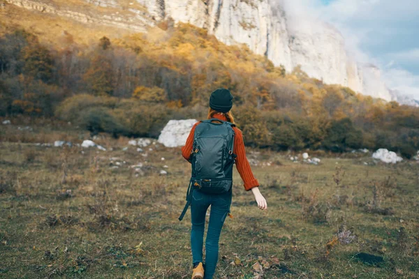 Un viajero en pantalones vaqueros suéter con una mochila en la espalda y un cálido sombrero montañas paisaje otoñal — Foto de Stock