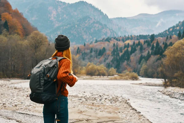 Un viajero con una mochila en un suéter y jeans están descansando en las montañas en la naturaleza cerca del río en otoño — Foto de Stock